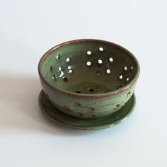 a green ceramic bowl with holes in the middle on a white table top next to a saucer