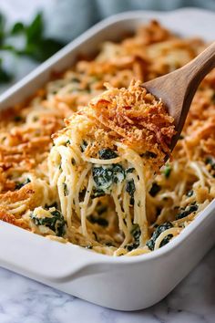 a casserole dish with spinach and cheese being lifted from the casserole