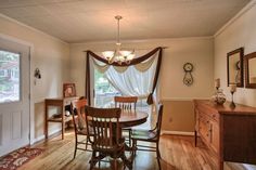 a dining room table and chairs in front of a window with drapes on it