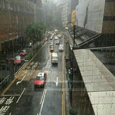 cars driving down a rain soaked street in the middle of an urban area with tall buildings