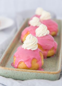 small pastries with pink icing and white frosting are on a green tray