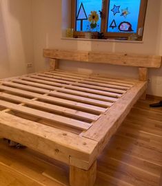 a bed frame made out of wood on top of a hard wood floor next to a window