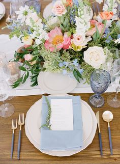 the table is set with blue and white plates, silverware, and floral centerpieces