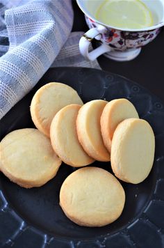 some cookies are on a black plate next to a cup of tea and a white cloth