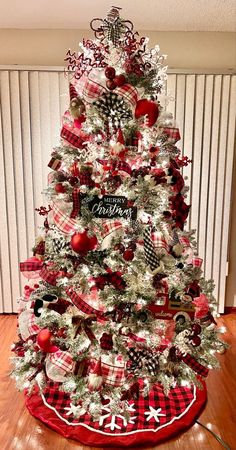 a christmas tree decorated with red, white and black plaid ribbon is on the floor