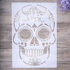 a paper cut out of a sugar skull on a wooden surface with flowers in the background