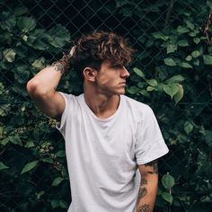 a man with tattoos on his arm standing in front of a chain link fence and looking off into the distance