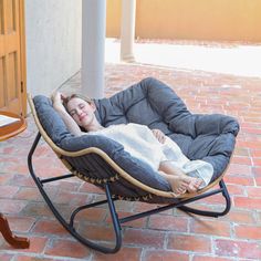 a woman is sleeping in a chair on the brick floor next to a wooden table