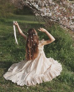 a woman in a dress sitting on the ground with her arms outstretched and flowers flying from her hair