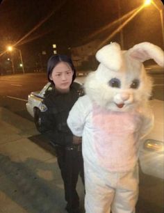 a woman standing next to a police officer in bunny costumes on the street at night