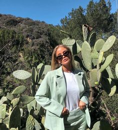 a woman standing in front of a cactus with her hands on her hips and wearing sunglasses