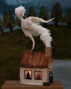 a white cat statue on top of a small house with trees in the back ground