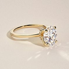 a yellow gold engagement ring with a round cut diamond in the center, on a white background