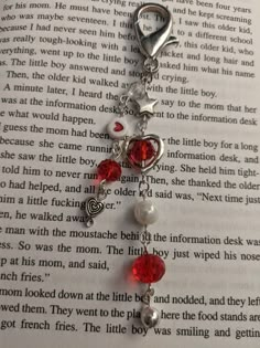 an open book with a red heart charm and pearls on it's side, sitting on top of a table