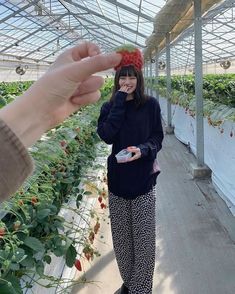 a woman standing in a greenhouse holding a strawberry