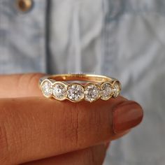 a woman's hand holding a yellow gold ring with five diamonds