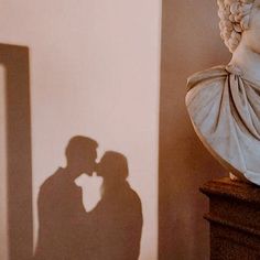 two people standing next to each other in front of a mirror with the shadow of a busturine on it