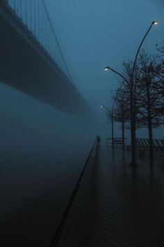 a person walking down a street in the fog with a bridge in the back ground