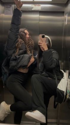 two women taking pictures in an elevator with their cell phones