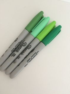 four pens sitting on top of each other in green and grey ink, lined up