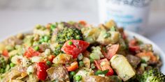 a white plate topped with broccoli, potatoes and other vegetables next to a cup of water