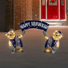 two lighted teddy bears holding a happy hanukkah sign in front of a building