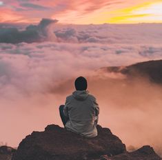 a person sitting on top of a mountain looking at the clouds