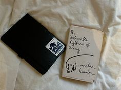 an open book with writing on it next to a small black notebook that is laying on a white sheet