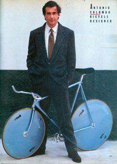 a man in a suit and tie standing next to a blue bicycle with wheels on it