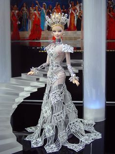 a barbie doll wearing a dress made out of wire and beads, standing in front of a staircase