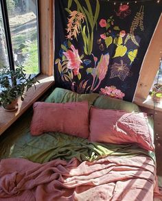 a bed with pink and green sheets in front of a large tapestry on the wall