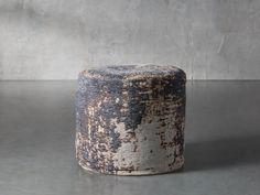 an old, worn out stool sits on a concrete floor in front of a gray wall