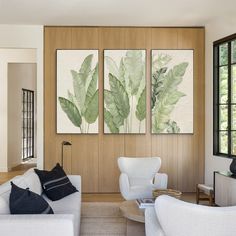 a living room filled with white furniture and paintings on the wall above it's windows