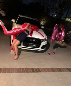 a woman leaning on the hood of a white car with a red ribbon tied to it