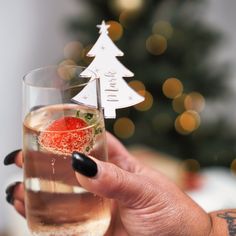 a woman holding up a wine glass with a strawberry in it and a christmas tree decoration on top