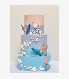 a three tiered cake with blue and pink frosting, decorated with seashells and starfish