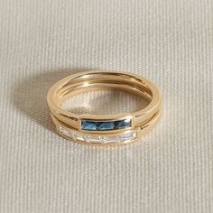 two gold wedding bands with blue and white stones on the sides, set against a beige background