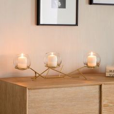 three lit candles sit on top of a wooden dresser in front of a framed photograph