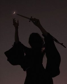 the silhouette of a woman holding an umbrella in the air with her hands up at night