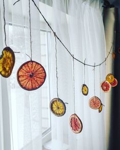 some fruit hanging from a string in front of a window with sheer curtains on the windowsill