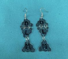 the earrings are made out of metal and have black letters on them, with silver hooks