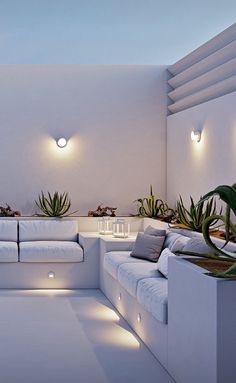 a living room with white couches and lights on the ceiling, in front of a plant