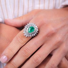 a close up of a person's hand wearing a ring with an emerald and diamond center