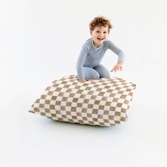 a little boy sitting on top of a pillow that is shaped like a checkerboard pattern