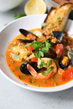 a bowl of seafood soup with bread and garnish on the side, ready to be eaten