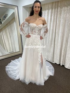 a woman standing in front of a mirror wearing a white wedding dress with sheer sleeves