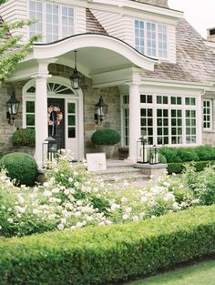 a house with white flowers in front of it and bushes around the front yard area