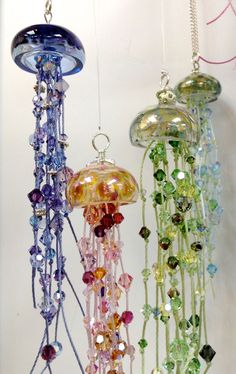 three glass wind chimes hanging from a white wall next to each other in different colors