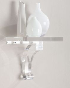 two white vases sitting on top of a glass shelf next to a wall mounted toothbrush holder