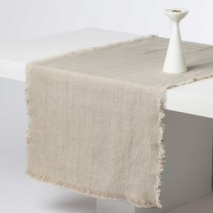 a white vase sitting on top of a table next to a beige cloth draped over it